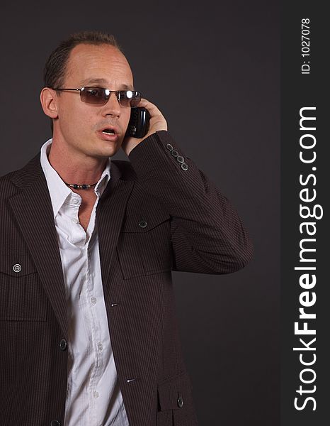 A man involved in a conversation on his cell phone, wearing a sportsjacket and sunglasses. A man involved in a conversation on his cell phone, wearing a sportsjacket and sunglasses