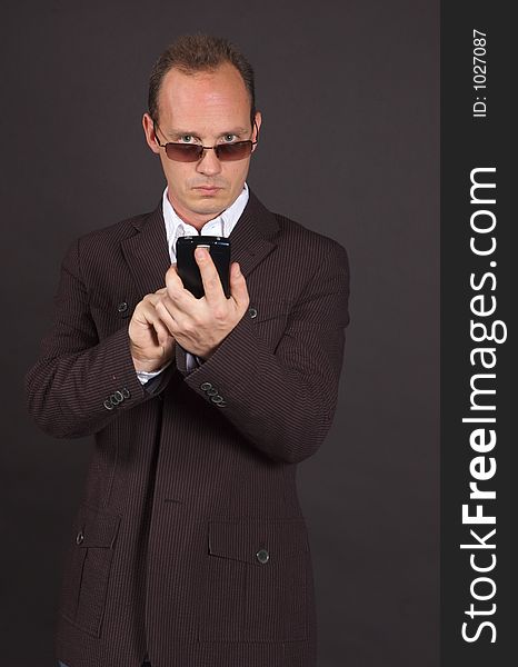 A man in a sportsjacket and sunglasses, punching in information to his mobile device. A man in a sportsjacket and sunglasses, punching in information to his mobile device