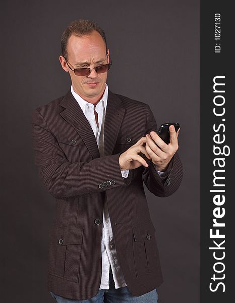 A man in a sportsjacket and sunglasses, punching data into his mobile device. A man in a sportsjacket and sunglasses, punching data into his mobile device