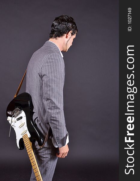 A man in a pinstriped suit with an electric guitar slung over his shoulder