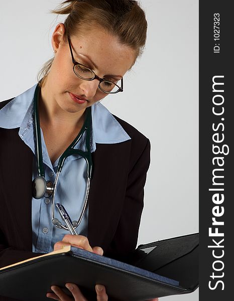 A woman in a business suit with a stethoscope around her neck, writing into a notepad. A woman in a business suit with a stethoscope around her neck, writing into a notepad