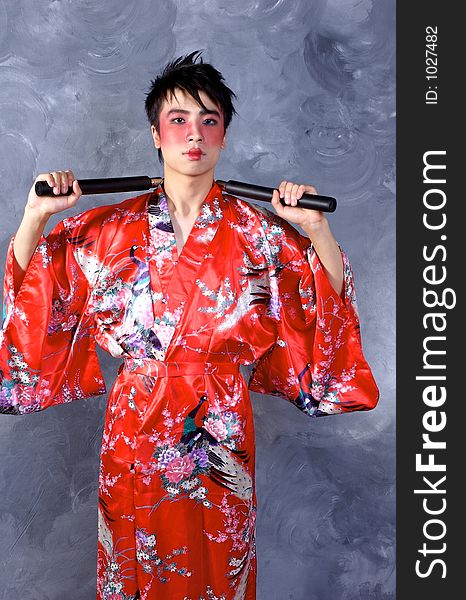 A man in a Geisha outfit, holding a set of Nunchaku. A man in a Geisha outfit, holding a set of Nunchaku