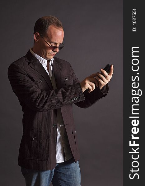 A man in a sportsjacket and sunglasses, punching in information to his mobile device. A man in a sportsjacket and sunglasses, punching in information to his mobile device