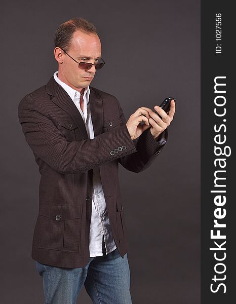 A man in a sportsjacket and sunglasses, punching in information to his mobile device. A man in a sportsjacket and sunglasses, punching in information to his mobile device