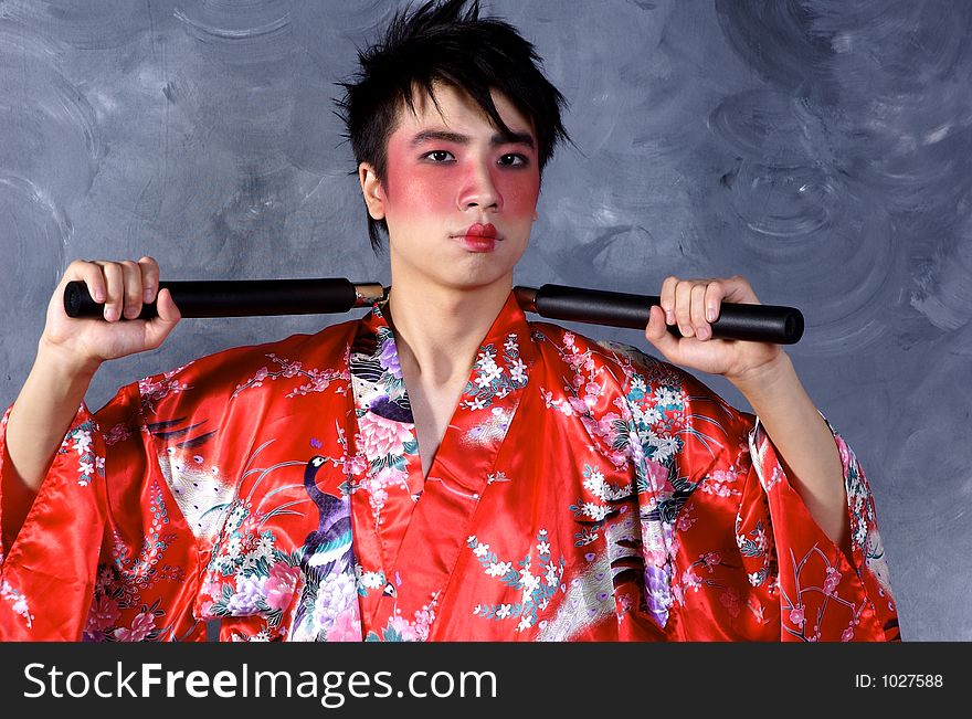 A man in a Geisha outfit, holding a set of Nunchaku. A man in a Geisha outfit, holding a set of Nunchaku