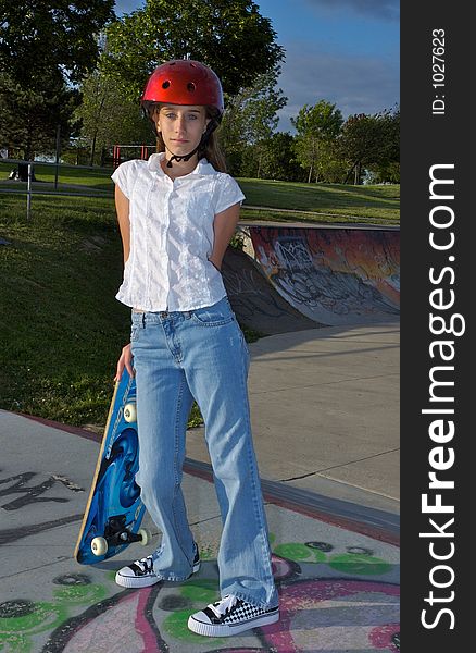A young girl leaning against her skateboard, wearing a helmet. A young girl leaning against her skateboard, wearing a helmet