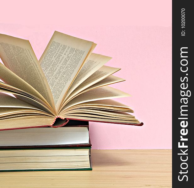 Open book and pile of books isolated on pink background