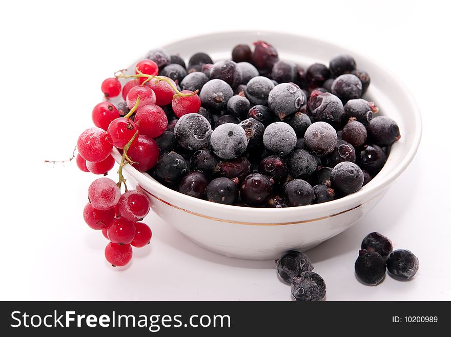 Bowl with frozen red and black currants on white