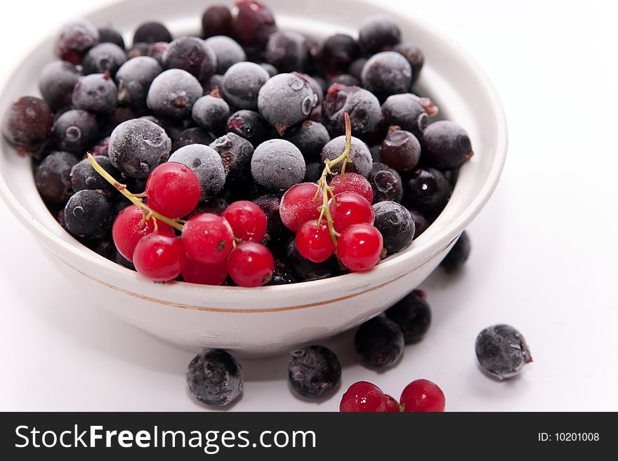 Bowl with frozen red and black currants on white