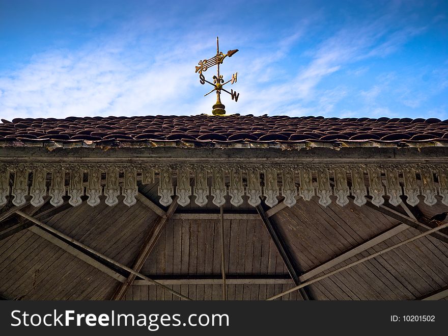 A vintage golden weather vane on the roof top of a colonial hut that retained its meticulous ornamental details. A vintage golden weather vane on the roof top of a colonial hut that retained its meticulous ornamental details.