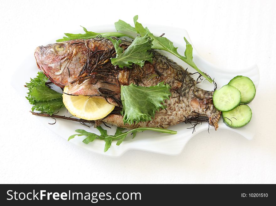 Grilled fish with greens lemon and cucumber on the plate over white