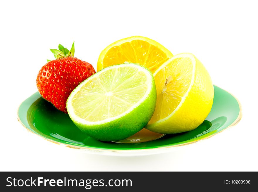 Lemon, lime and orange halves on a fancy green plate with a red juicy strawberry on a white background. Lemon, lime and orange halves on a fancy green plate with a red juicy strawberry on a white background