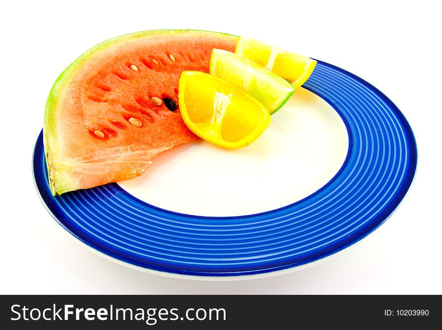 Slice of red juicy watermelon with a lemon, lime and orange wedge on a blue plate with a white background. Slice of red juicy watermelon with a lemon, lime and orange wedge on a blue plate with a white background