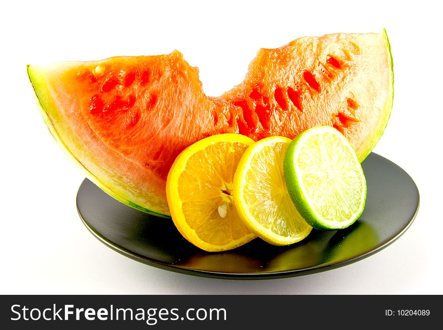 Slice of red juicy watermelon with a slice of lemon, lime and orange on a black plate with a white background. Slice of red juicy watermelon with a slice of lemon, lime and orange on a black plate with a white background