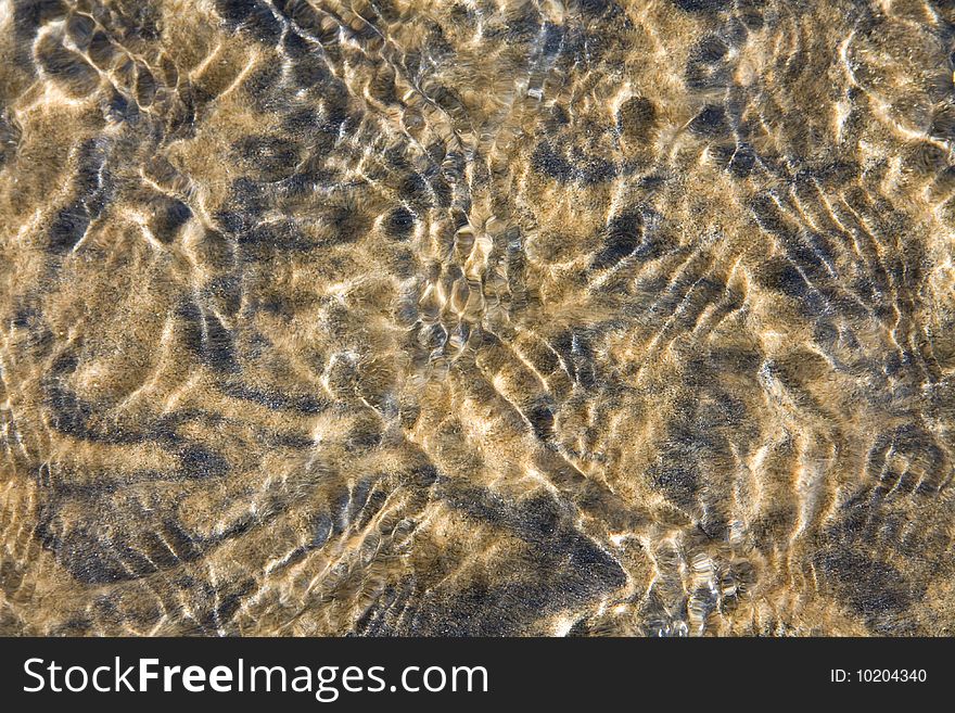 Closeup of clear water flowing over black and yellow sand forming patterns and ripples. Closeup of clear water flowing over black and yellow sand forming patterns and ripples