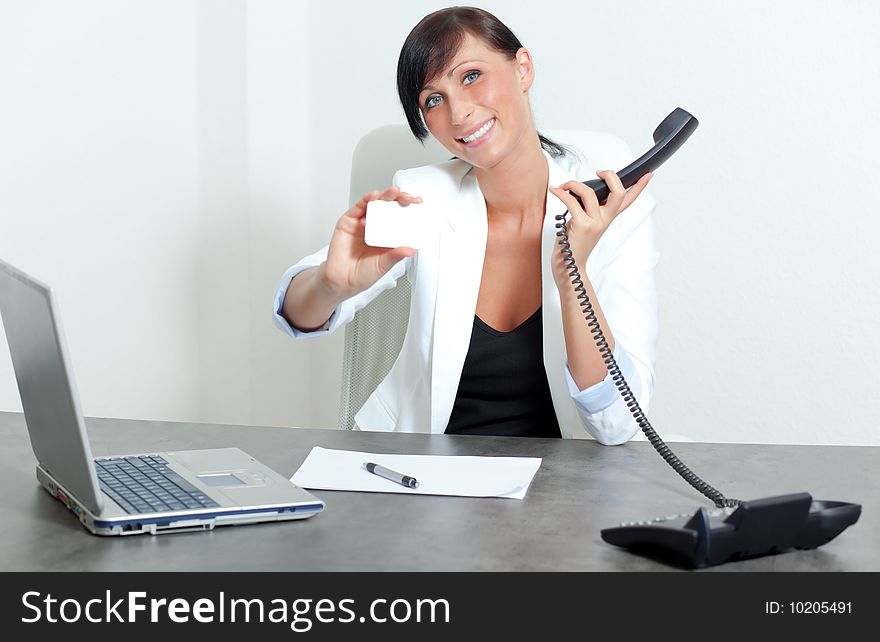 Office woman sitting and holding blank businesscard smiling on table and telephone
