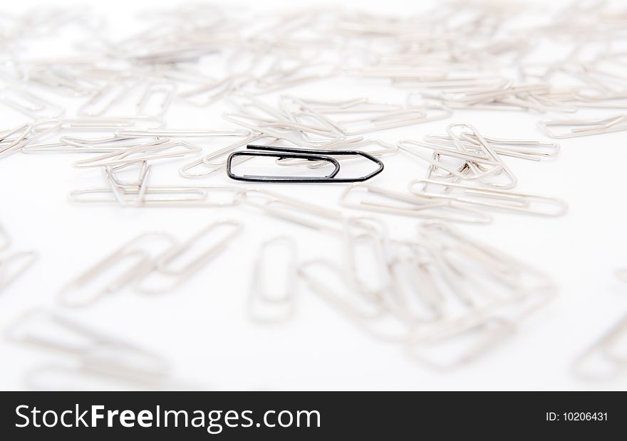 One black paperclip among many steel grey paperclips on white background. One black paperclip among many steel grey paperclips on white background