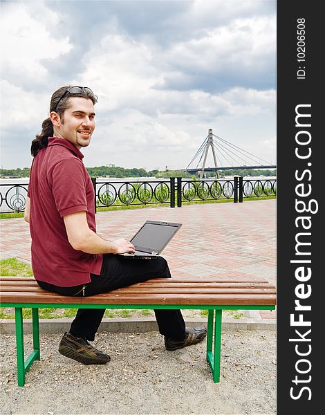 Young man sitting on a park bench with his laptop. Young man sitting on a park bench with his laptop
