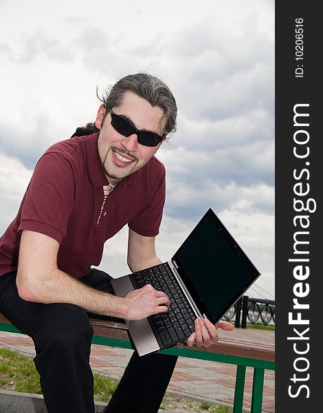 Young man sitting on a park bench with his laptop. Young man sitting on a park bench with his laptop