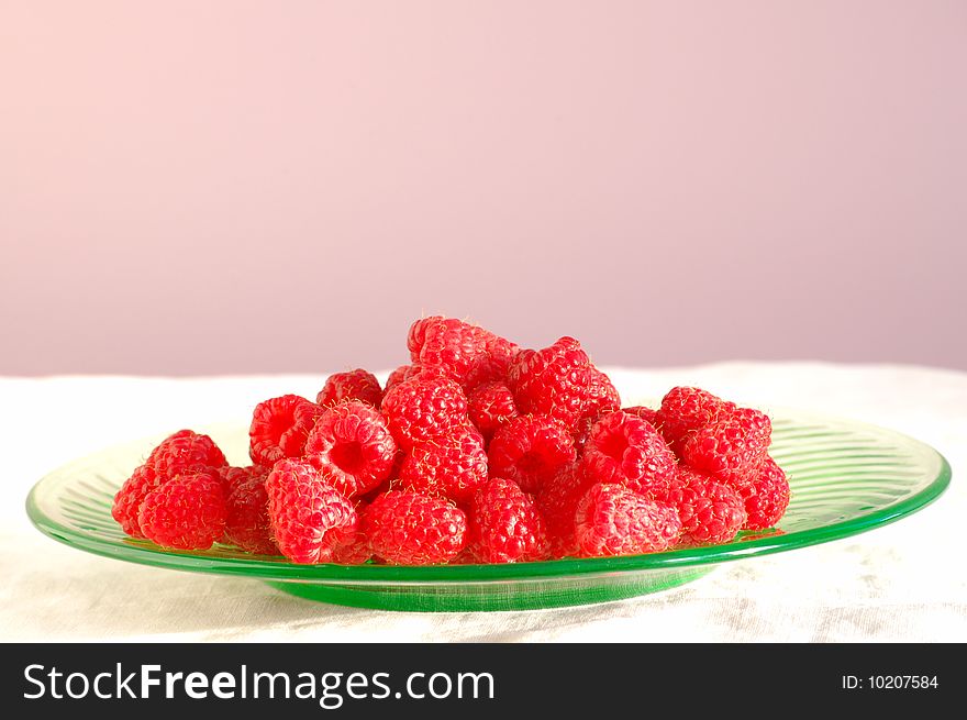 Delicious summer raspberries sit on a green glass plate, with a purple background. Delicious summer raspberries sit on a green glass plate, with a purple background.
