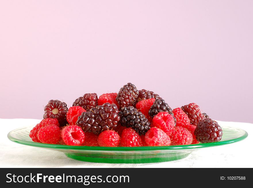 A luscious mound of blackberries and raspberries sits on a green glass plate, with a purple background.