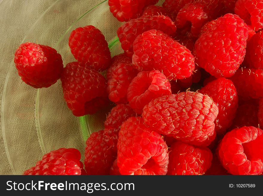 Red raspberries spill onto a green glass plate.