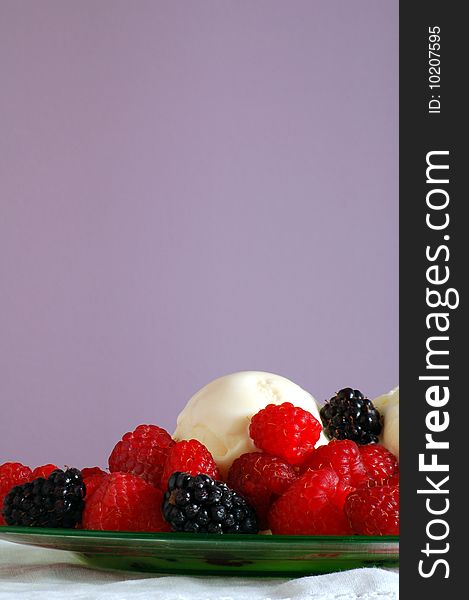 Vanilla ice cream is topped with red raspberries and blackberries, with a purple background.  Portrait orientation. Vanilla ice cream is topped with red raspberries and blackberries, with a purple background.  Portrait orientation.