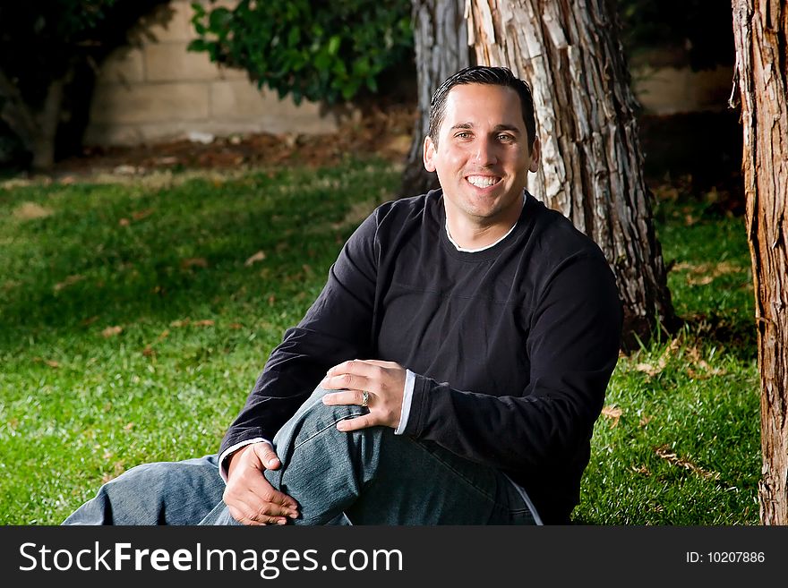 Portrait taken of a cheerful man sitting on the grass.