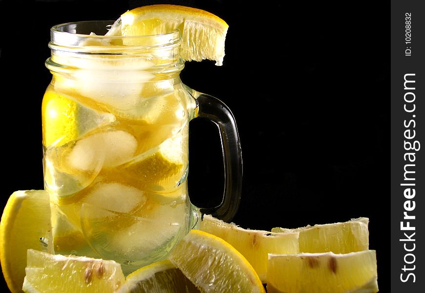 A glass mug of lemonade with ice cubes and lemon wedges