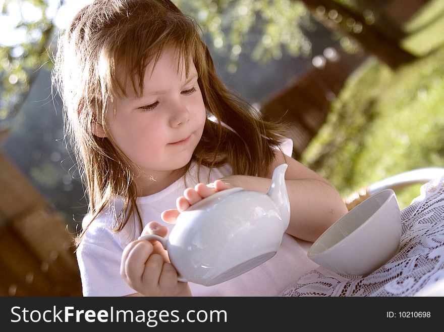 The beautiful  little girl pours hot tea in a cup