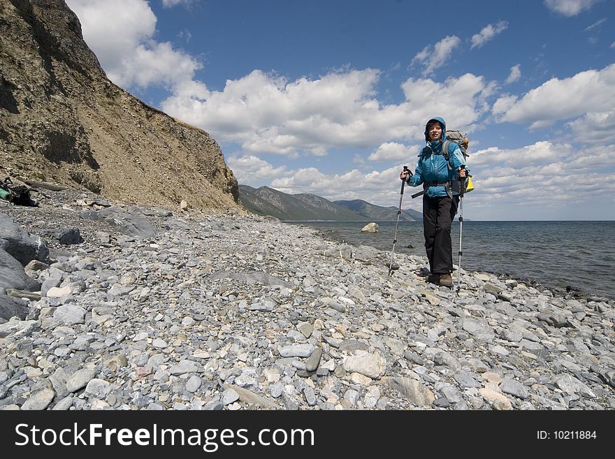 Woman backpacker goes on a coast. Lake Baikal, Eastern Siberia. Woman backpacker goes on a coast. Lake Baikal, Eastern Siberia