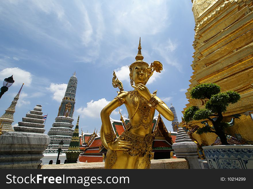 A golden thai angel statue and monument towers inside grand palace in Bangkok