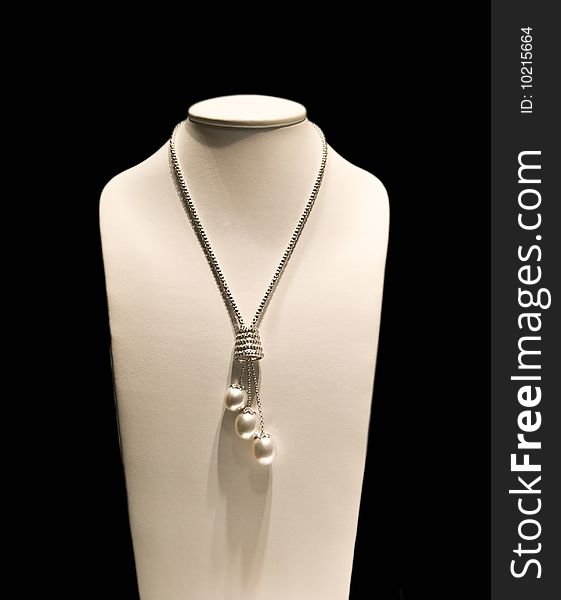 A silver jewelry necklace hung on a model isolated on a black background. A silver jewelry necklace hung on a model isolated on a black background.