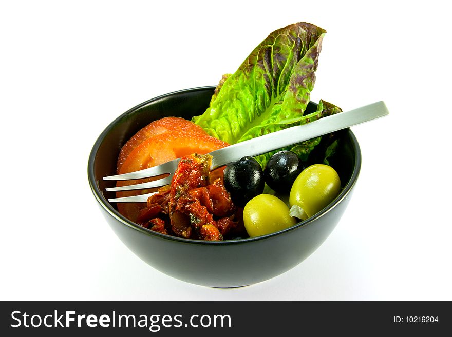 Black bowl with tomatoes, lettace and green and black olives and a small fork on a white background. Black bowl with tomatoes, lettace and green and black olives and a small fork on a white background