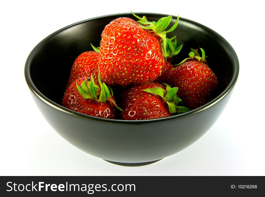 Whole red ripe strawberries in a black bowl on a white background