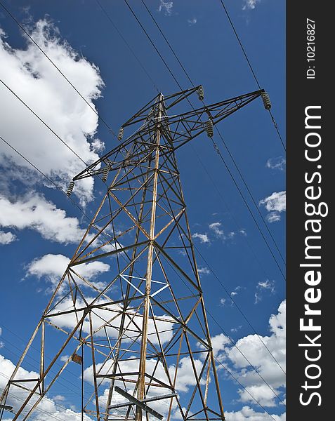 Bottom-up view of a rusty power line mast against blue sky and white clouds