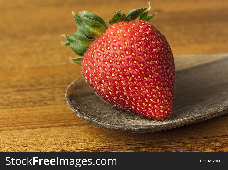 A single strawberry on an old wooden spoon. A single strawberry on an old wooden spoon