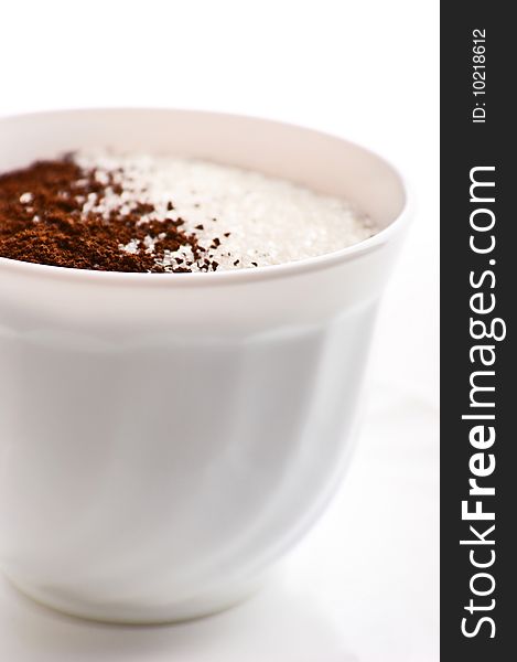 Cup with ground coffee inegrating into sugar is isolated over a white background. Cup with ground coffee inegrating into sugar is isolated over a white background