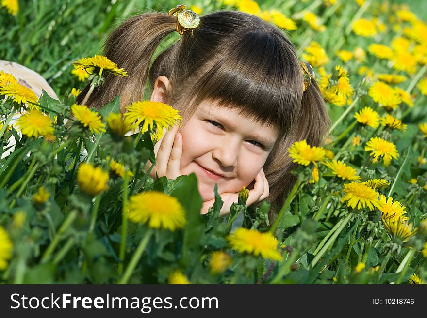 Little cute girl is lying on the dandelion meadow
