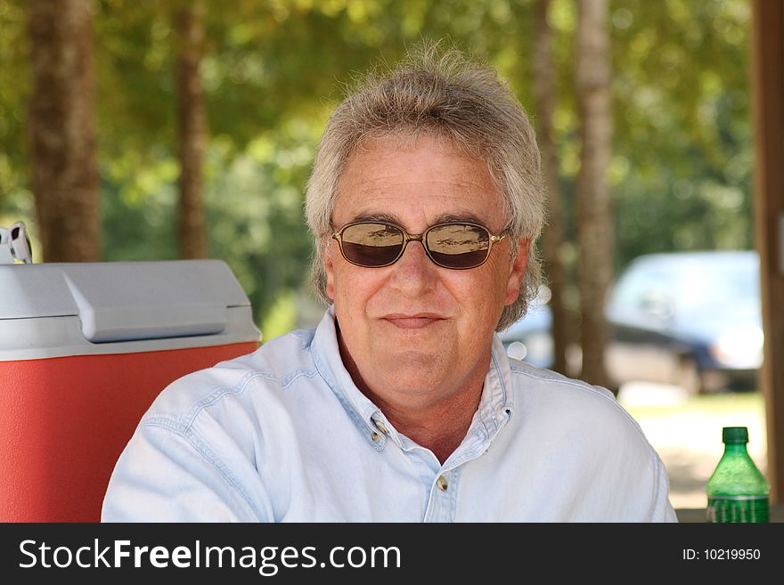 Baby boomer man smiling with gray hair and glasses in park. Baby boomer man smiling with gray hair and glasses in park