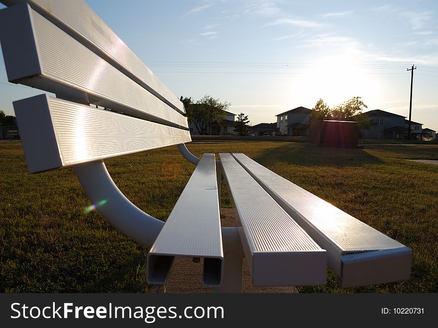 This park bench looks at a basketball court in Altus, OK.  The sun and houses in in the background light up the seat of the bench. This park bench looks at a basketball court in Altus, OK.  The sun and houses in in the background light up the seat of the bench.