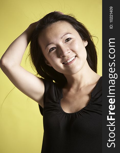 Young Asian woman standing against a yellow background pulls back her hair from her face. Young Asian woman standing against a yellow background pulls back her hair from her face.