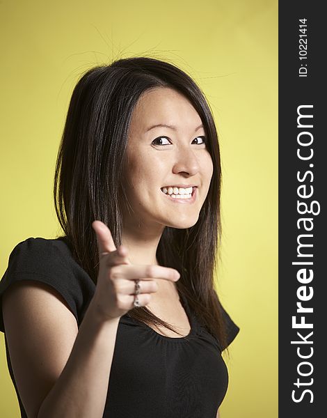 Young Asian woman weraing a black t-shirt pretends to shoot viewer with her index finger and flashes a cheesy smile. Young Asian woman weraing a black t-shirt pretends to shoot viewer with her index finger and flashes a cheesy smile.