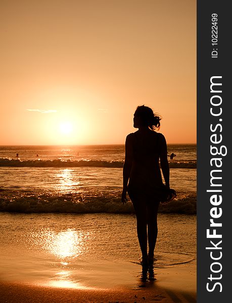 A pretty girl stands at the oceans edge looking at the setting sun. A pretty girl stands at the oceans edge looking at the setting sun.