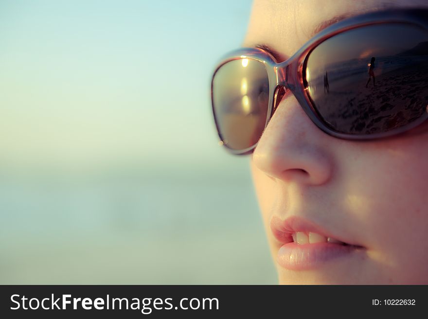 A gorgeous girl looks out over the beach and waves and her sunglasses reflect the scene. A gorgeous girl looks out over the beach and waves and her sunglasses reflect the scene.