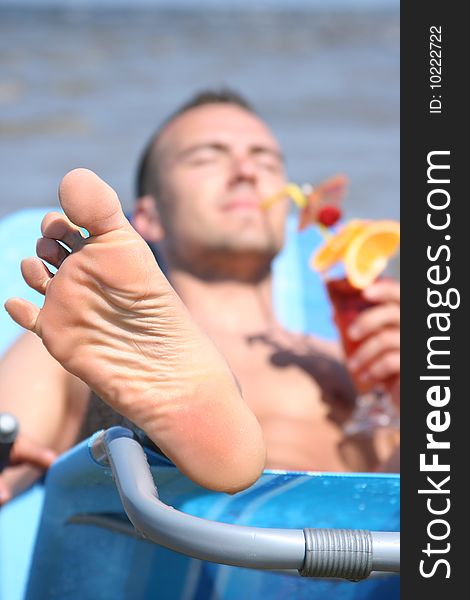 Young guy relaxing with cocktail (focuc on foot)