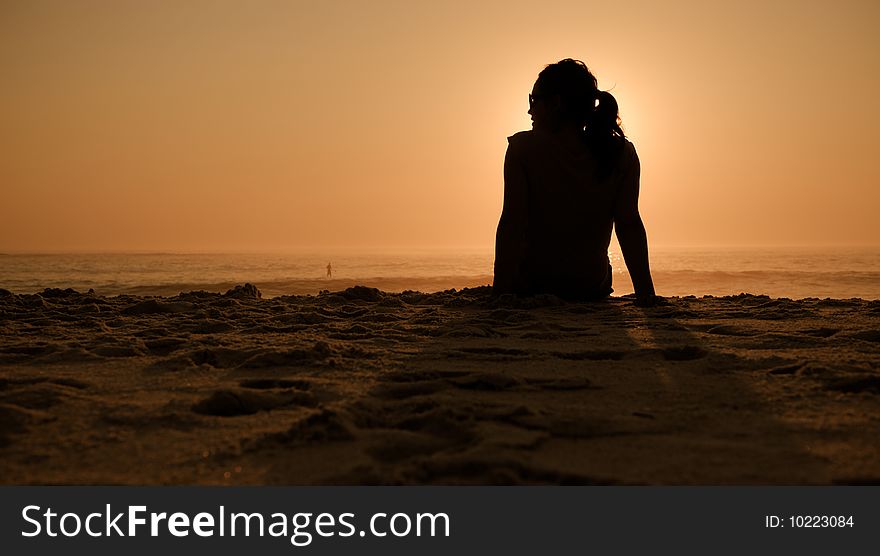 A pretty girl watches the waves at the beach during sunset. A pretty girl watches the waves at the beach during sunset.