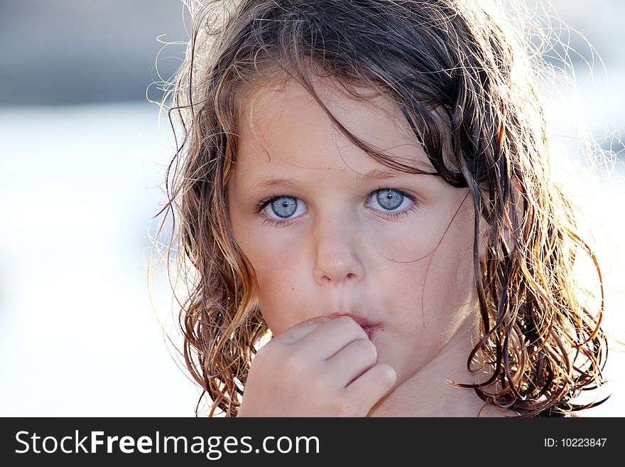 A child with hand up to her mouth eating crisps on a beach with crumbs all over her face. A child with hand up to her mouth eating crisps on a beach with crumbs all over her face