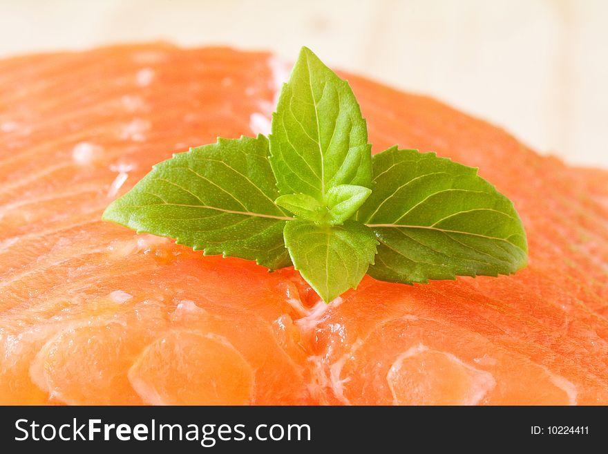 A piece of fresh raw salmon with basil leaves