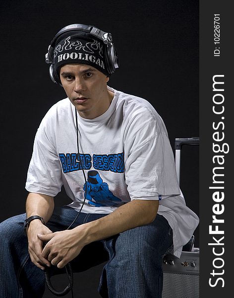 Young DJ/rapper sitting on his mobile sound system isolated on black background